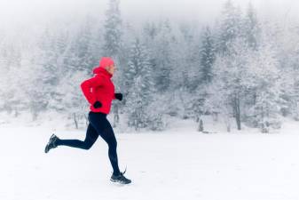 Trail running woman in winter mountains. Sport, fitness inspiration and motivation. Young happy woman cross country running in mountains on snow, winter day. Female trail runner jogging outdoors.
