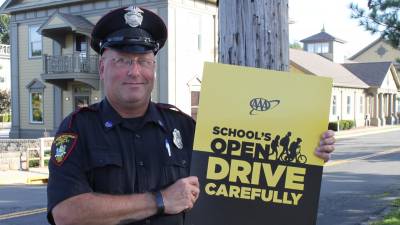 Village of Goshen school crossing guard Bill Scheuermann is pictured placing a poster from the American Automobile Association's School's Open -- Drive Carefully safety campaign.