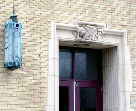 Art Deco lantern and sculpted relief over the door featuring a globe, a book with crossed quill pens in front, and an hourglass