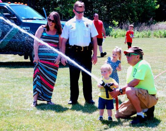 A Chester firefighter lets Charlie Doellinger, age one and a half, shoot the firehose. His three-year-old sister, Katherine, awaits her turn with mother, Julia, and father, Chester Police Chief Daniel Doellinger (Photo by Ed Bailey)