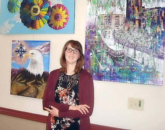 Goshen artists following where the road leads Exhibit Curator Michele Marie Meek with several of the larger pieces of artwork; to her right is Meek’s “Unity in Diversity” and on her left is “Kingsbridge Wonderland” by Jennifer Charton. (Hot-Air Balloons painting has been sold, by the way.)
