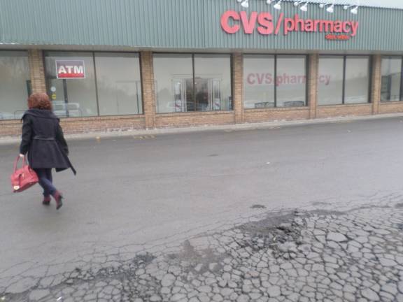 A shopper walks past the crumbling pavement of the Goshen Plaza Shopping Center on a rainy Wednesday (Photo by Nathan Mayberg)