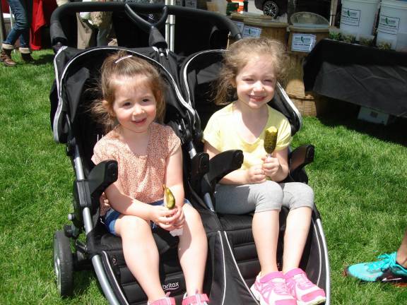 Fresh is back Emilia, 2, and her sister Lucy, 5, are each enjoying a “pickle on a stick,” which, along with beef jerky, are their favorites at the Farmers’ Market. They’re at the market with their mom, Melanie Muccari from Montgomery, and grandmother Nancy Eustace of Goshen. (Photo by Geri Corey)