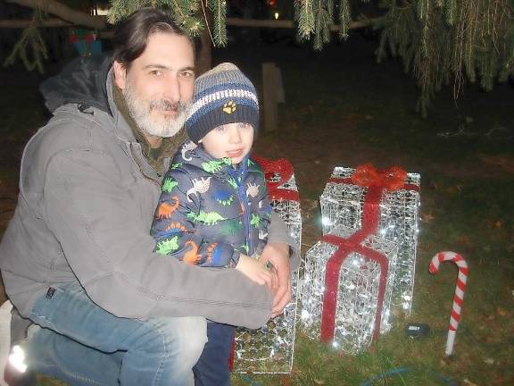 Lloyd LeBaron sits comfortably with his son, Logan LeBaron, 3, under the newly lit Christmas tree during the tree lighting in Goshen Village Park.