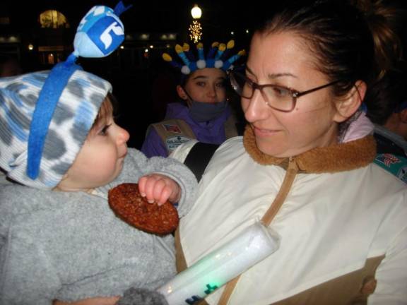 Oliver Kopolovich, who was born on Hanukkah last year, is happy to be celebrating with a yummy latke. He’s here with his mom, Marissa, who comes every year to Goshen from Campbell Hall to the celebration. Photos by Geri Corey.