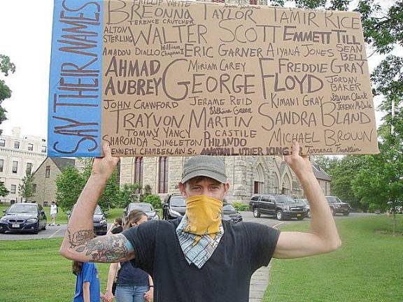 Scott Martens, from Minisink, held up a handmade sign, listing many names of people who lost their lives by violent means. The other side of the sign read: “Ending Racism Starts at Home. Teach Your Children Well. Photo by Geri Corey.