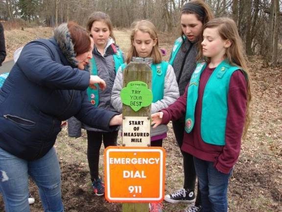 With help from Leader Nicole Petrakis, the Girl Scouts of Troop 551 in Goshen nail their plaques with words of encouragement on a mile marker post on the Heritage Trail. From left, the girls are Aubrey Rampulla, Nera Weinstein, Rhiannon Petrakis and Lucy Attreed. One of their plaques is shown on the front of the post. (Photo by Geri Corey)