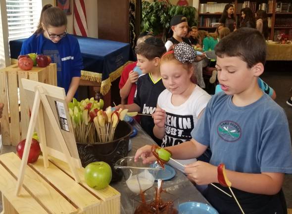 All are welcome at High Holiday Services and children’s programs at Chabad Apples in Honey: Brady Crowe of Washingtonville demonstrates the Rosh Hashanah tradition of dipping apples in honey, as Isabella Hauck of Middletown looks on, at a Chabad Hebrew School High Holiday fair.