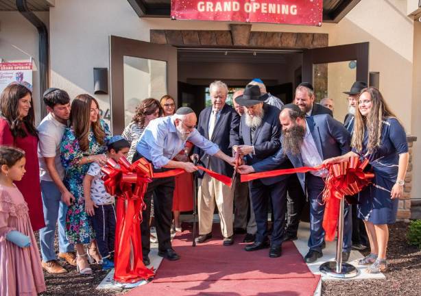 Cutting the Ribbon for the new Chabad Center for Jewish Life (l-r): Rosie and Sonia Young, Duvy, Chana and Kovy Burston, Shifra and Arthur Gellman, Tawnya Muhlrad (behind), Chabad President Gil Goetz, Monroe Village Mayor Neil Dwyer, Elias Muhlrad (blocked), Rabbi Moshe Kotlarsky from Chabad World Headquarters, Tzvi Gellman, Rabbi Pesach Burston, Dr. Pinny Young (partially blocked), Rabbi Efraim Mintz of Chabad World Headquarters, Simmie Gellman