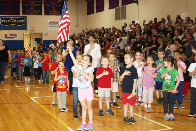Smiles, giggles at Kindergarten Festival Chloe Mosquera holds the American flag during the Pledge of Allegiance.
