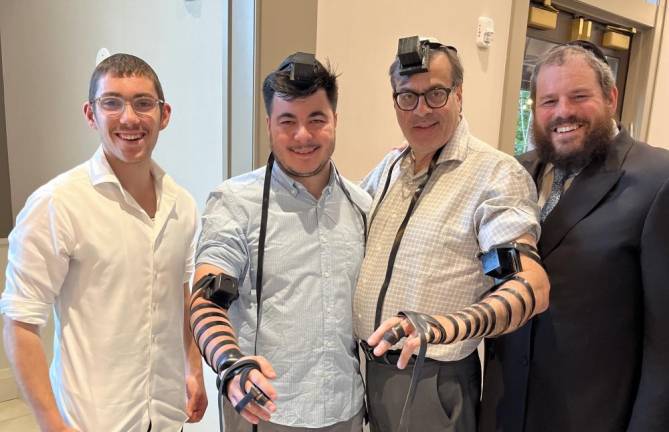 Father and son Elliot and Jesse Meshulam, of Highland Mills, don Tefillin as an extra mitzvah in honor of Israel at Chabad of Orange County’s Unity Shabbat event at the Chabad House in Monroe. Pictured with them are Rabbi Pesach Burston, right, and his son, Yossi Burston, left.