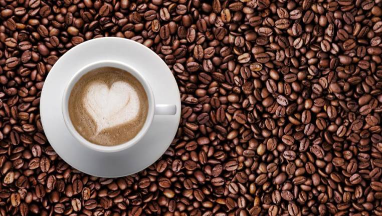 Top view - Coffee cup of LATTE ART Love symbol lover sign on top Pile of brown coffee beans with copy space for text or graphic design. Cafe' latte cream on top coffee in heart shape on background of raw coffee beans