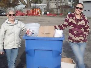 <b>Goshen residents Betsy Dunlevy on the left and Christine Cullen Schepps flank a Village of Goshen recycling bin, showing some acceptable recycling items, like the clean rigid plastic juice and water bottles, cardboard and paper. They’re asking village residents to read over the “Recycling Guide” before tossing items in the bin to help keep village costs down.</b>