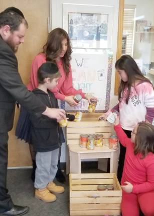 Rabbi Pesach and Chana Burston, along with Chabad Hebrew School students Landon Goldenberg of Warwick, Isabel Redling of Warwick and Libby Einav of Monroe place canned food in the donation baskets at Chabad. Thy will be used Dec. 23 to form a Can-orah that will then be donated to local food pantries.