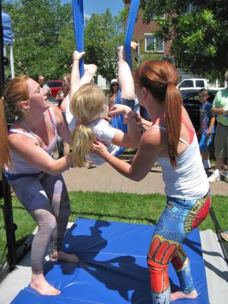 Katie Adams (left) and Katie Struble (right) help Anna Lisa Miely get into the aerial yoga silk.