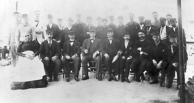 Undated photo of the Hudson River Steamer Mary Powell crew posing on deck with Captain A.E. Anderson, center front row with newspaper. First row: Fannie Anthony stewardess; fourth from left, Pilot Hiram Briggs; fifth, Capt. A.E. Anderson (with paper); sixth Purser Joseph Reynolds Jr. Standing, third from left: Barber (with bow tie). Black men at right possibly stewards. Photo from the Donald C. Ringwald collection, Hudson River Maritime Museum.