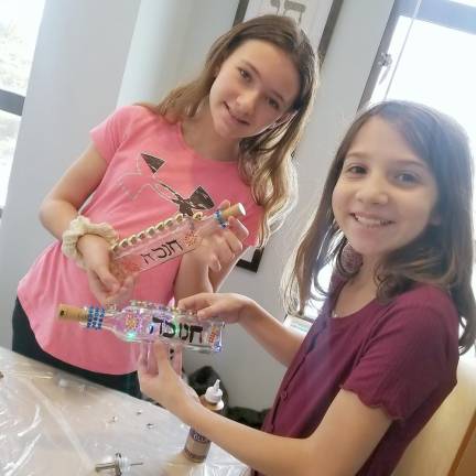 Hebrew School students Kaylie from Harriman and Lizzie from Monroe display the olive-oil-bottle light-up menorah they created.