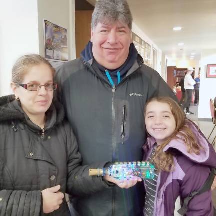 Chabad Hebrew School students Alana Scrank of Goshen proudly shows her parents, Rachel and David, the olive-oil-bottle light-up menorah they created while learning about Chanukah and the miracle of the oil.