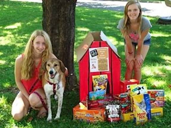 Darcy McDowell (left) and Hallory McBride show off the dog and cat food they’ve collected for their Girl Scout project, the Pet Food Pantry. With them is Clarice, Darcy’s one and a half year-old pet, who’s certainly pleased with the project. (Photo by Geri Corey)