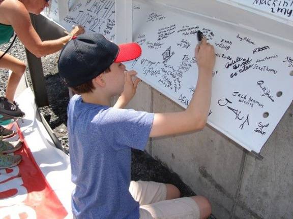 Jack Meek, a Goshen seventh-grader and avid library user, signs the beam before it was lifted to complete the steel framework for the new library. “It’s cool to have the names up there for as long as the building is standing,” said Jack. He’s hoping the library will have lots of history books, especially those on World War I and World War II (Photo by Geri Corey)