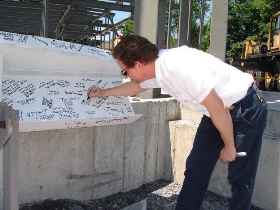 Matthew Gomm, library director, is pleased to sign the beam that will remain with the building as long as it exists. The beam was lifted to the top to complete the new building’s steel framework (Photo by Geri Corey)
