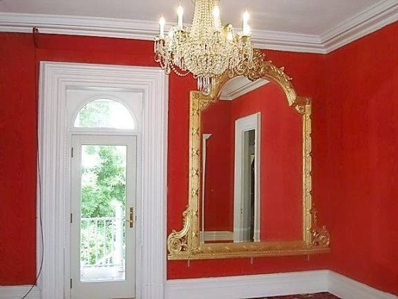 The Victorian parlor with fabric walls, thick crown and floor molding, and lavish mirror and chandelier.