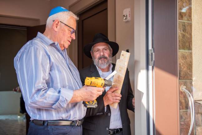 Elias Mulrad of Goshen and Chabad Gabbai Dr. Ira Kanis of Monroe affixing the mezuzah on the front door of the new Chabad Center for Jewish Life.