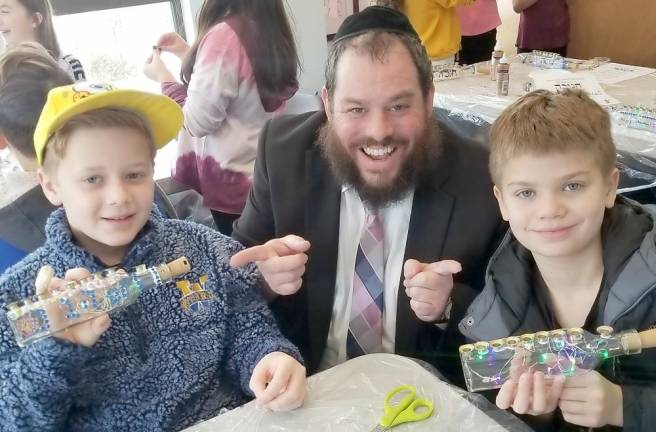 Hebrew School students Owen from Washingtonville and Jaden from Monroe are pictured with Rabbi Pesach, display the olive-oil-bottle light-up menorah they created.